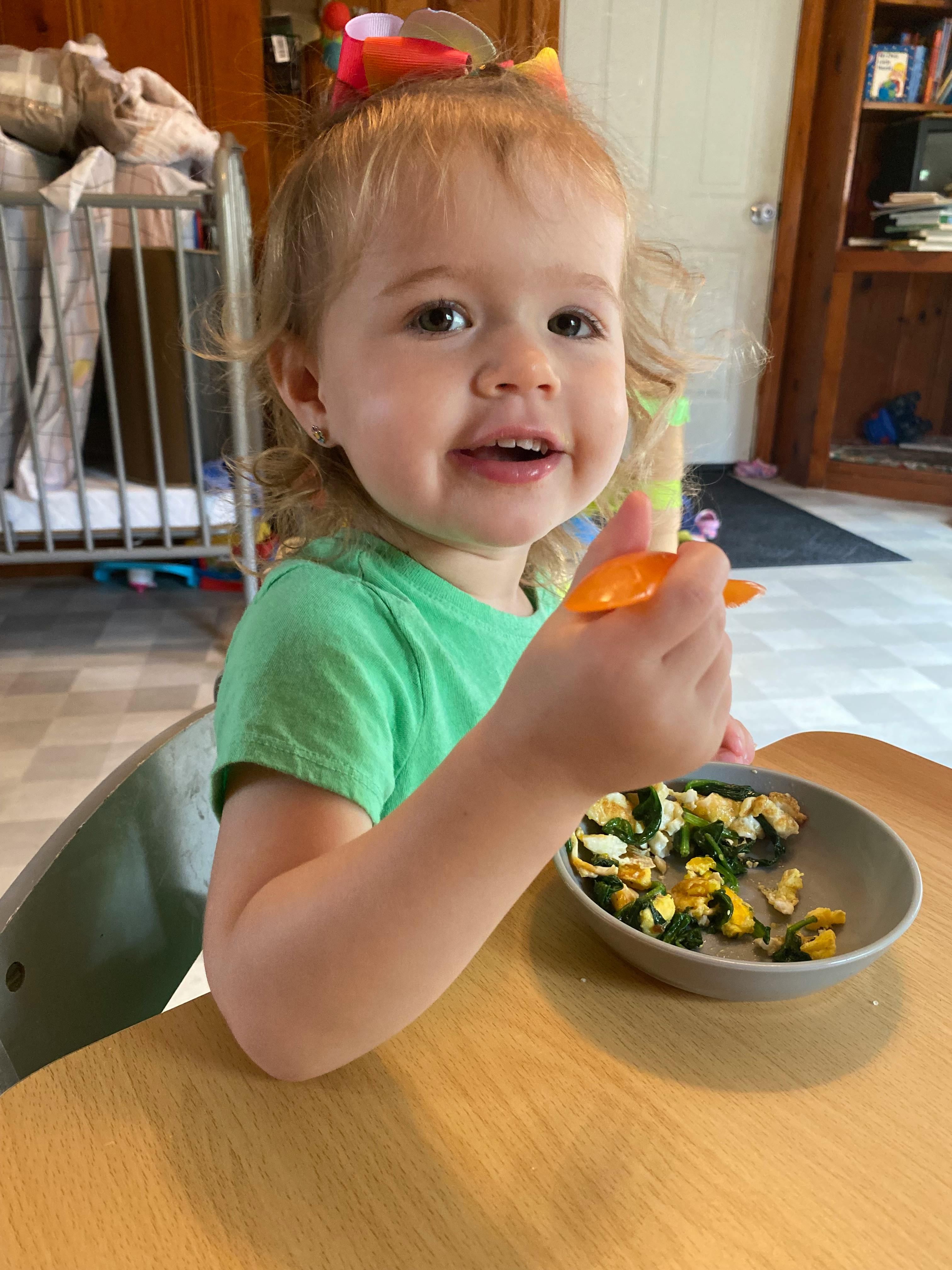 Child in a high chair holding a spoon with a bowl of food