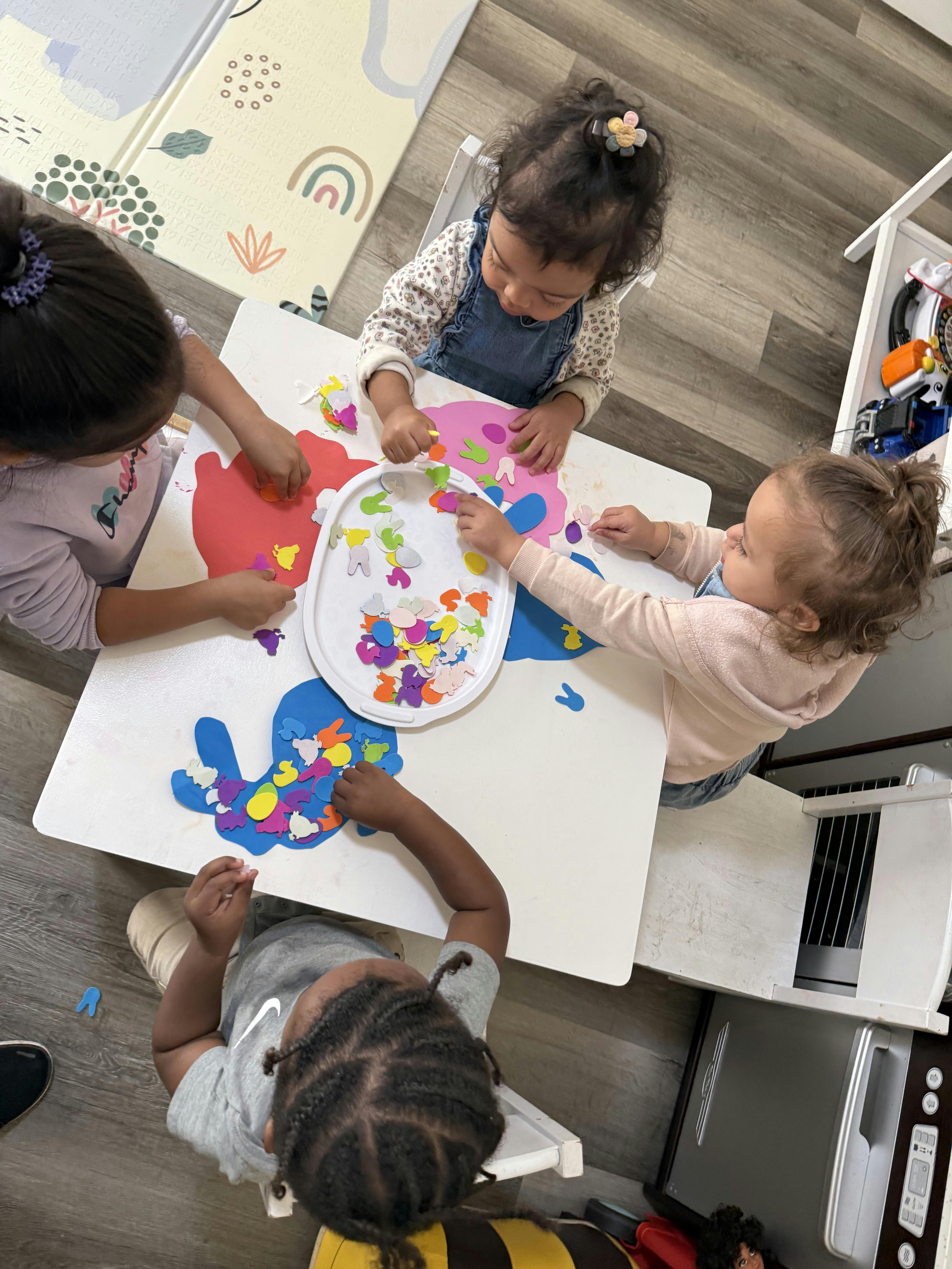 Four children sitting around a table placing colorful shapes on paper