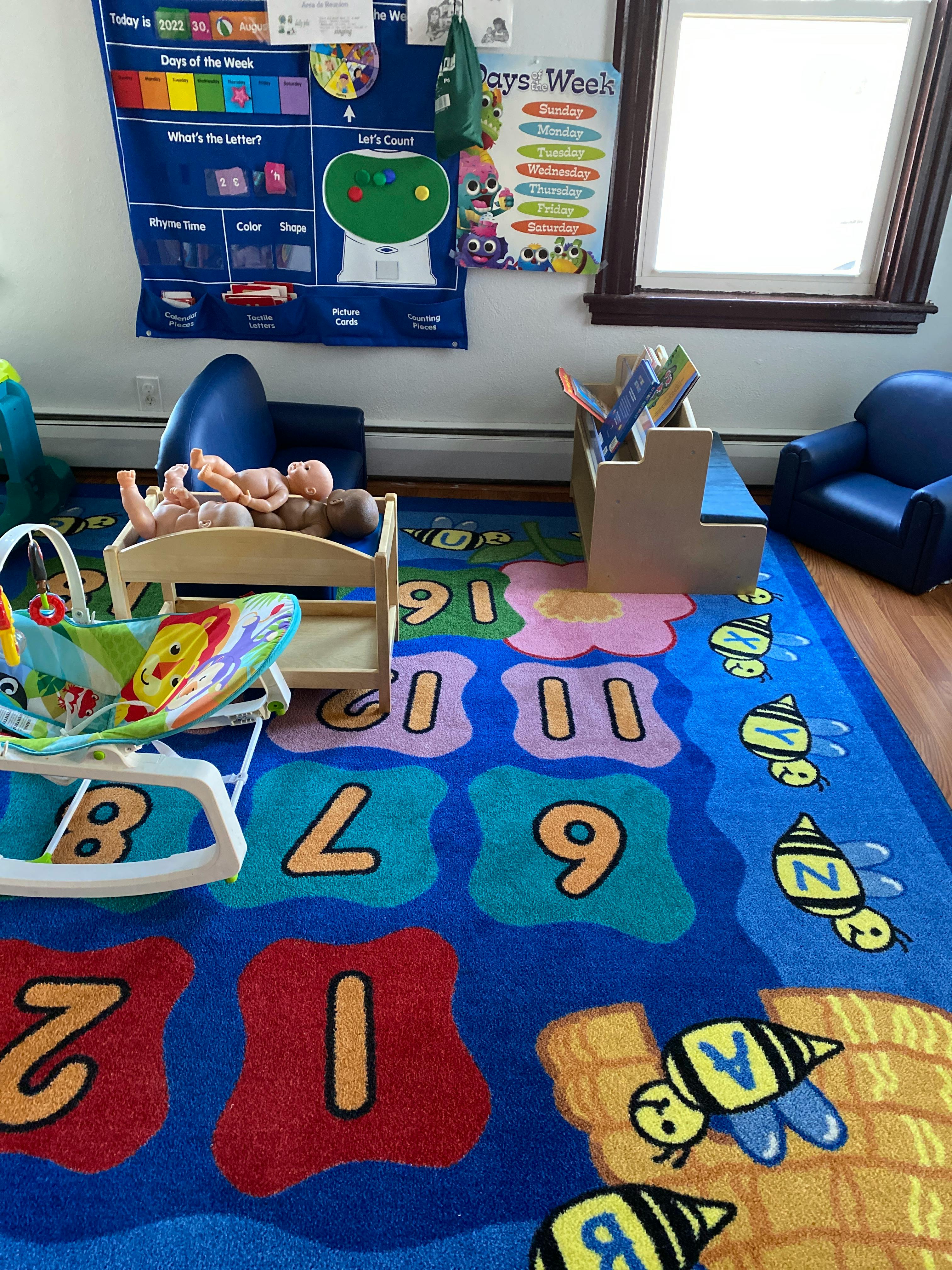 Dolls in a crib and a baby bouncer on a number and letter rug in a classroom