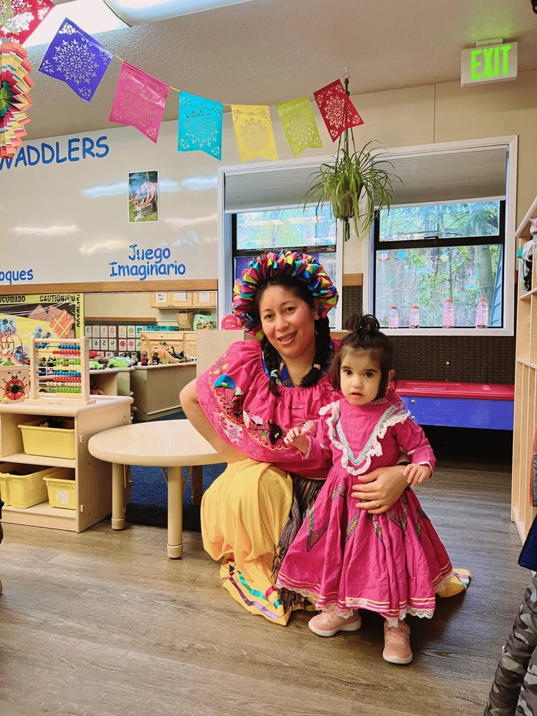 Adult and child in colorful traditional dresses in a preschool classroom