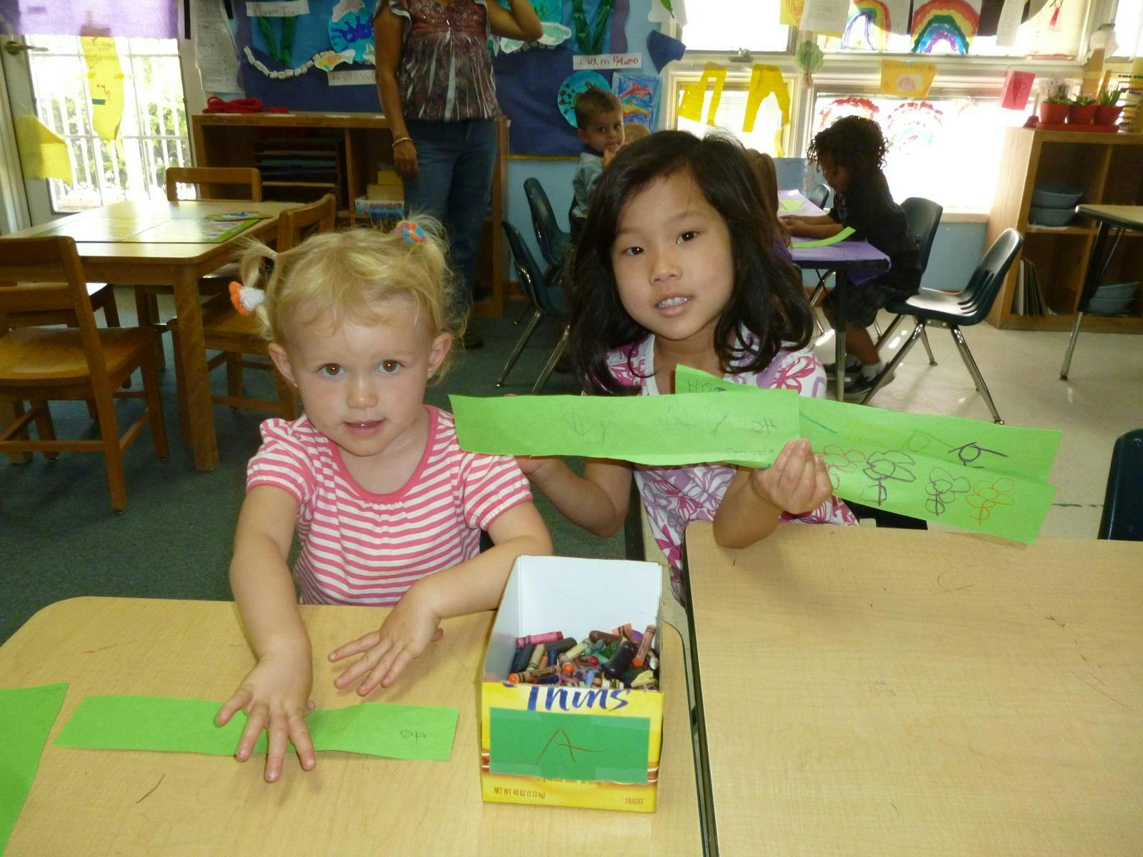 Two children at a table with green paper crafts in a classroom