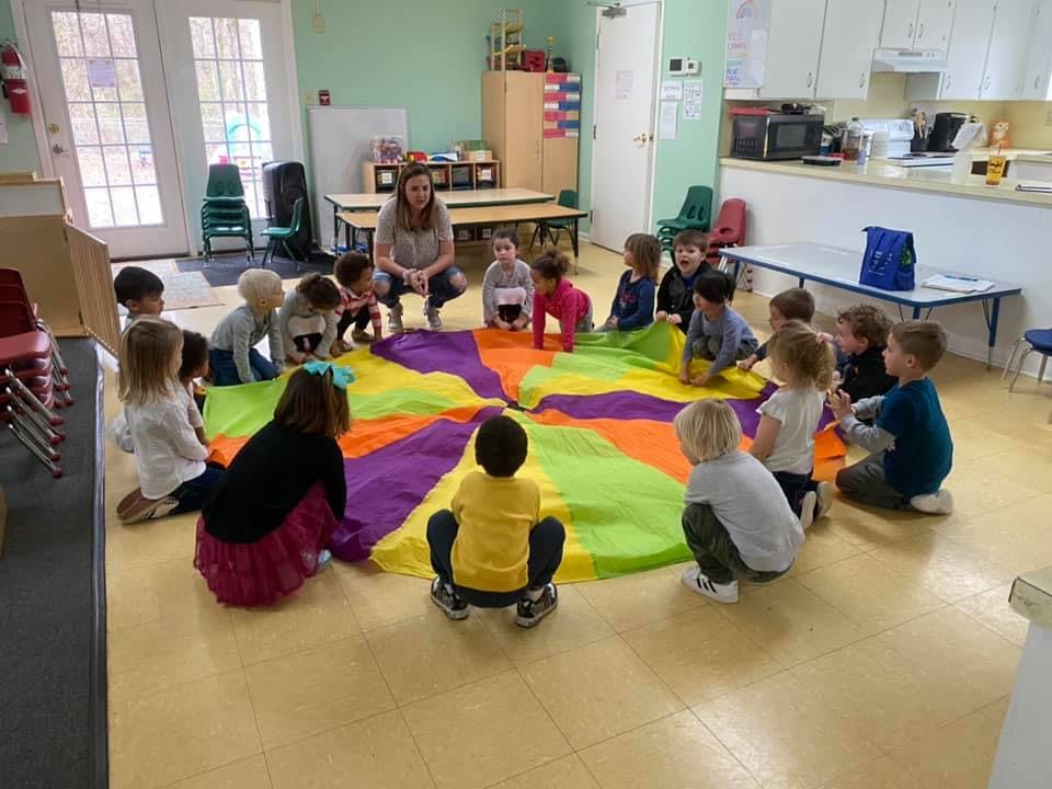 Adult and children sitting around a colorful parachute on the floor