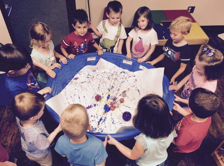 Children gathered around a sensory table with paint and objects