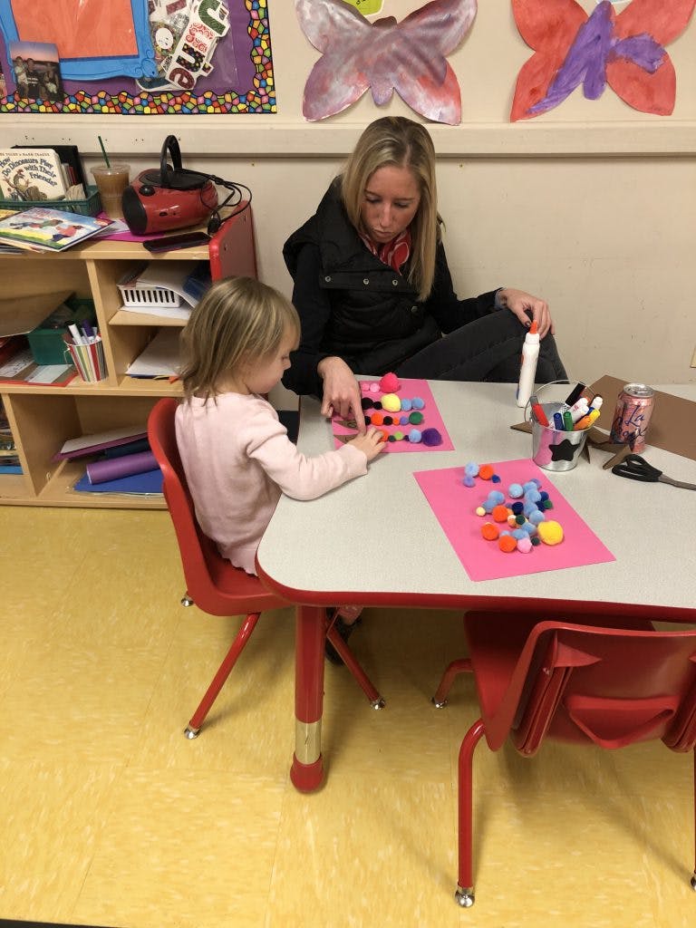 Adult and child doing a craft with pom-poms at a table