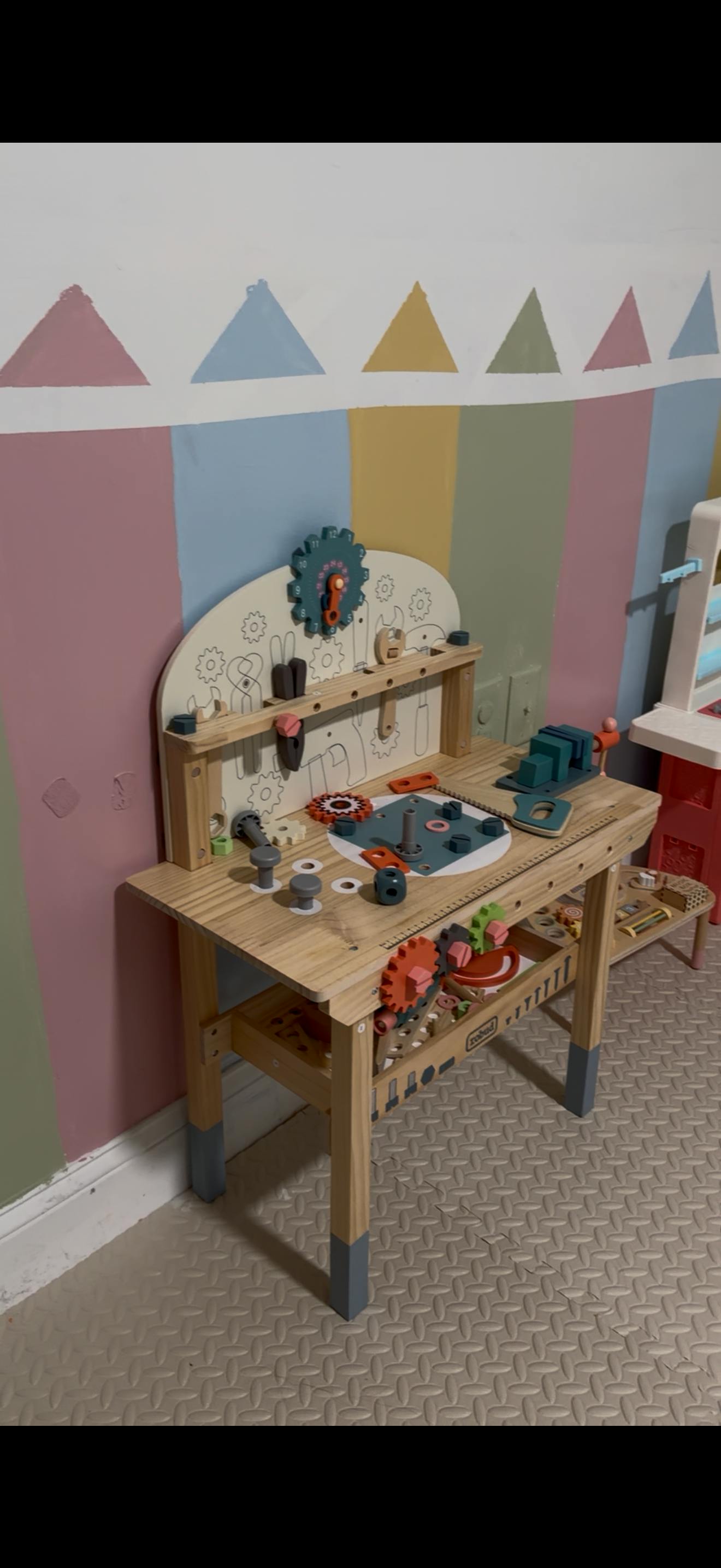 Wooden toy workbench with tool accessories against a patterned wall