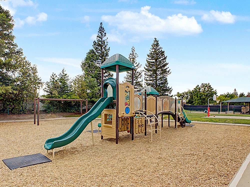 Playground with green and tan play structure, slide, and wood chip ground