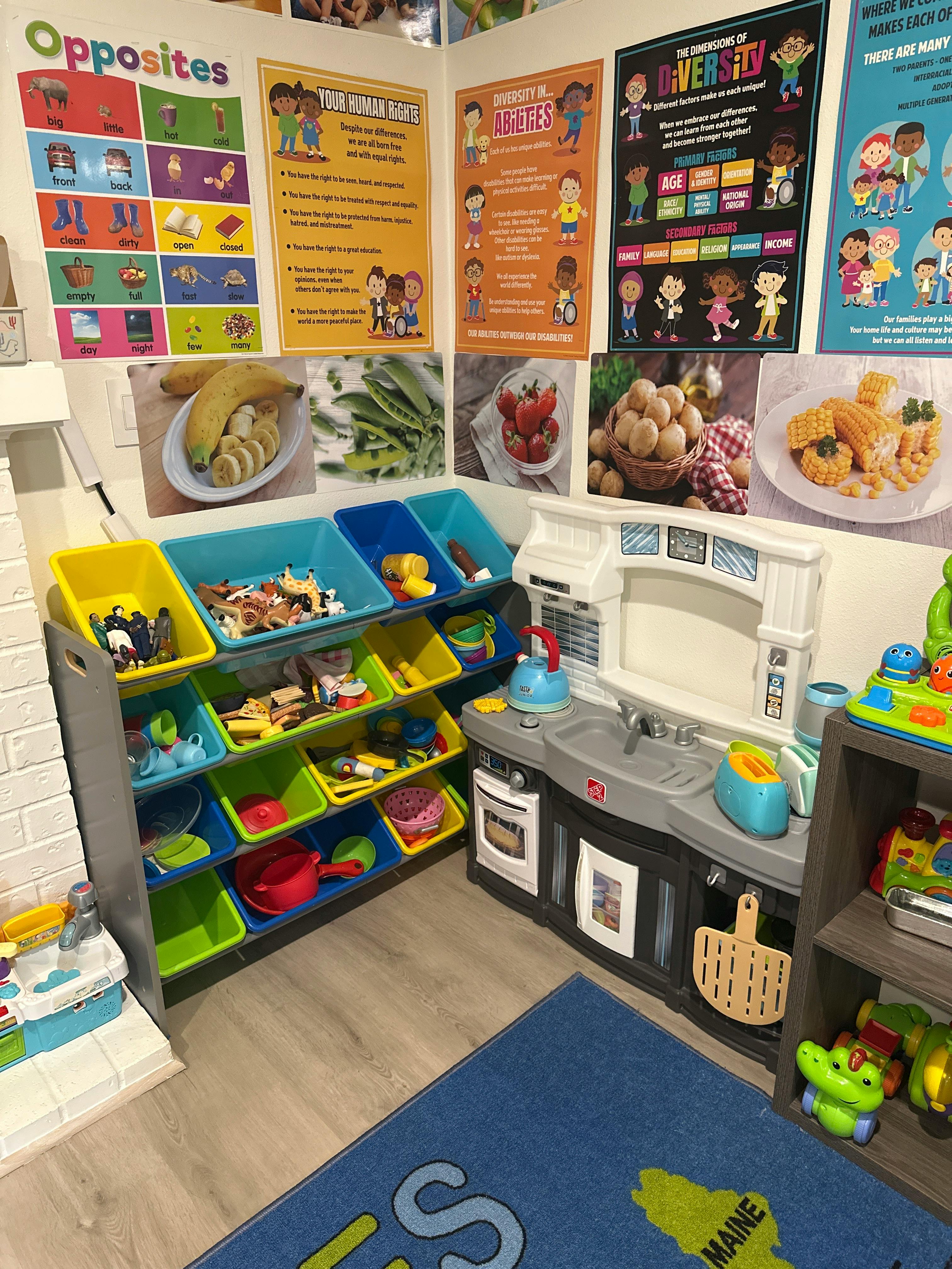 Play kitchen with toy storage bins next to educational posters on a wall