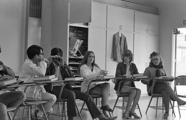 Students sitting at desks in a classroom, one person holds a camera