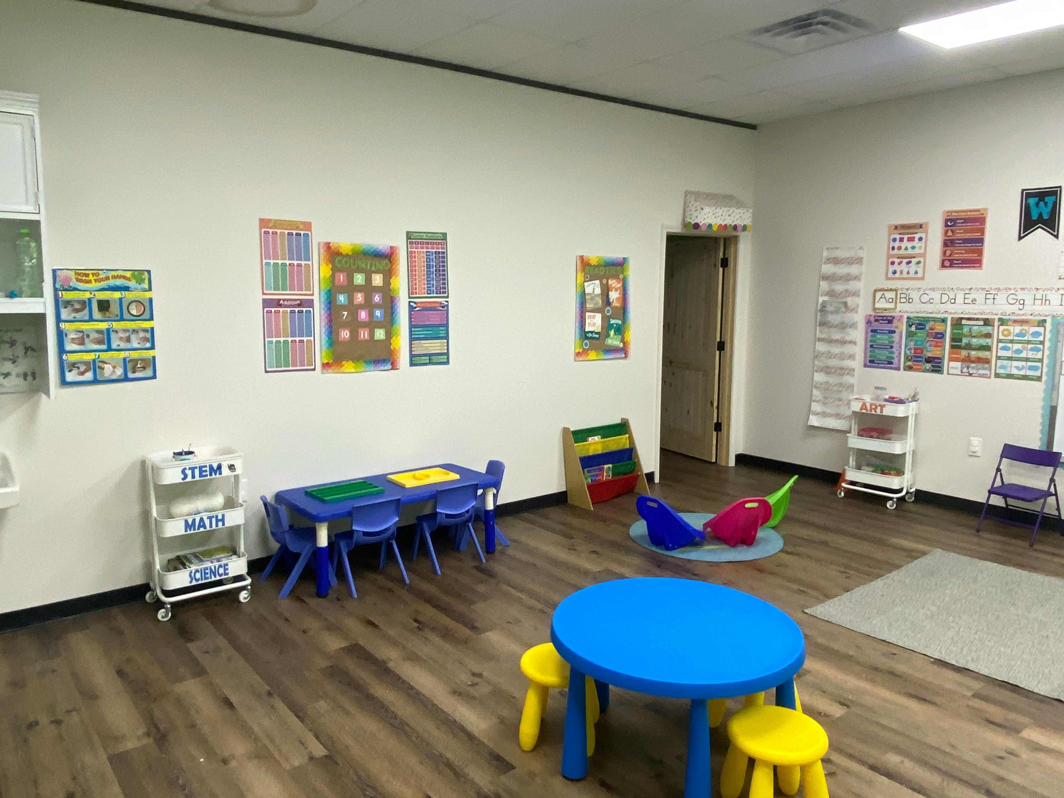 Classroom with small blue tables and chairs, educational posters on walls