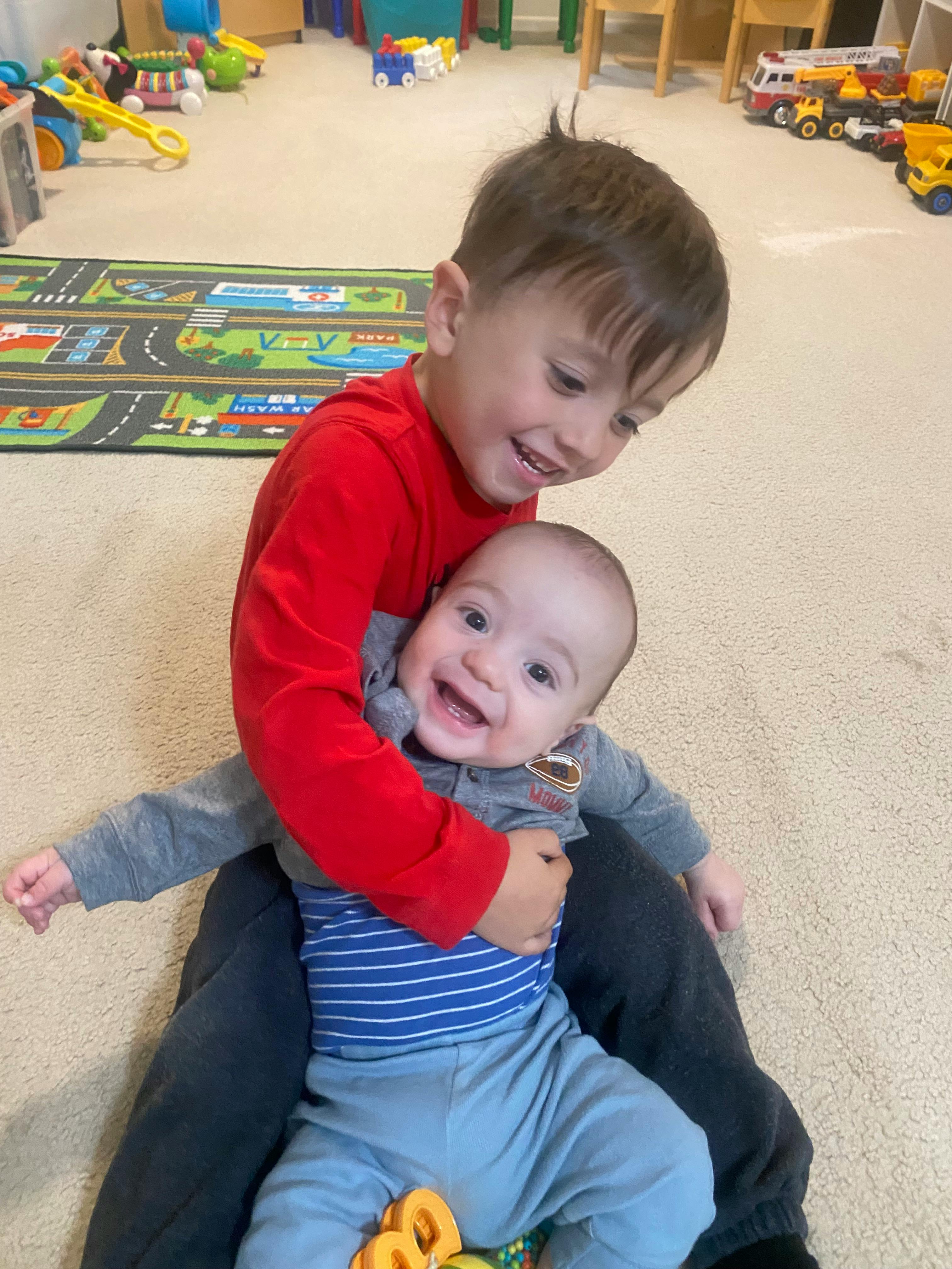 A young child holding an infant on a carpeted floor