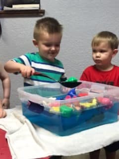 Two children playing with toys in a bin of water