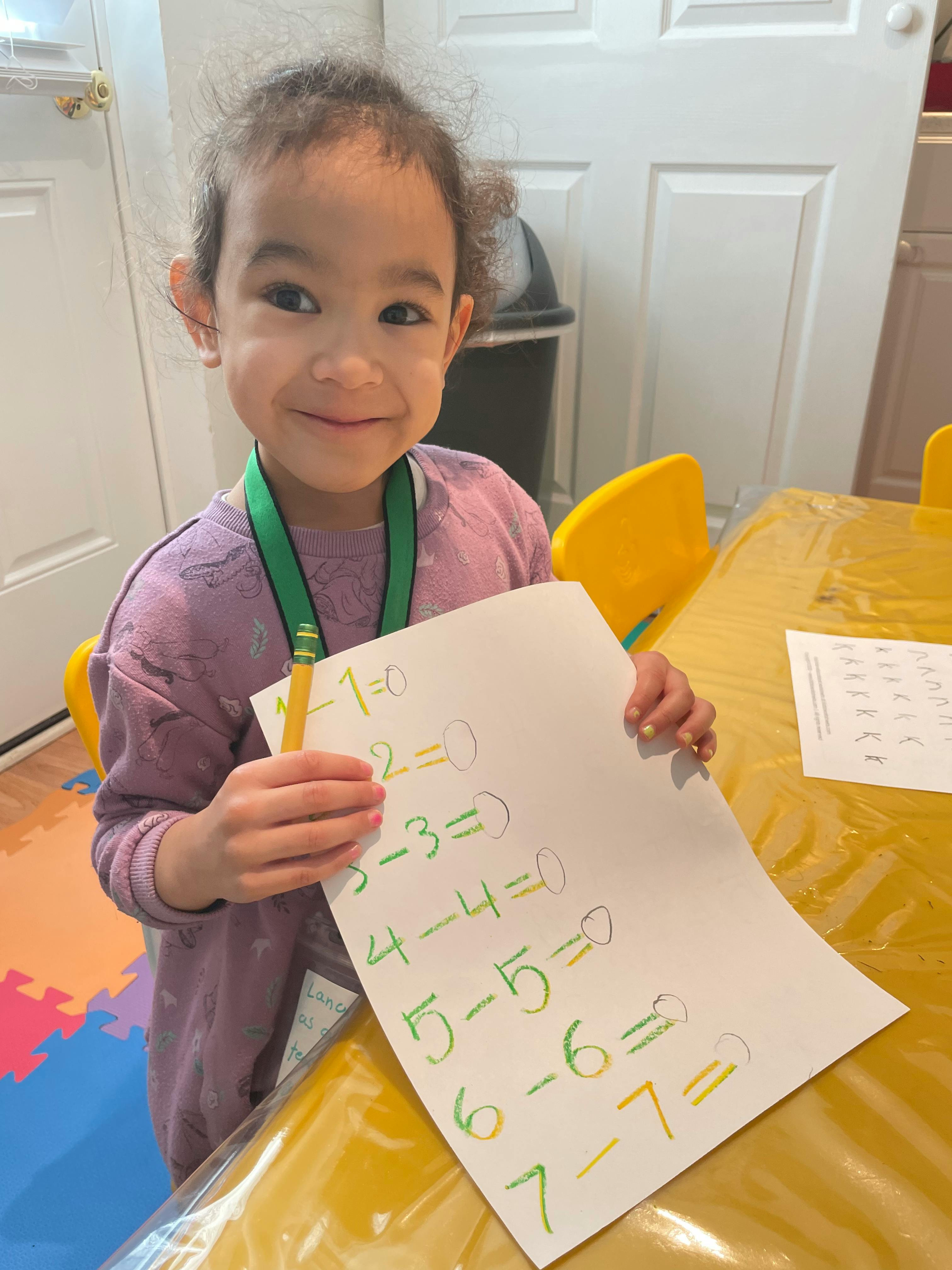 Child holding a paper with math problems and a pencil