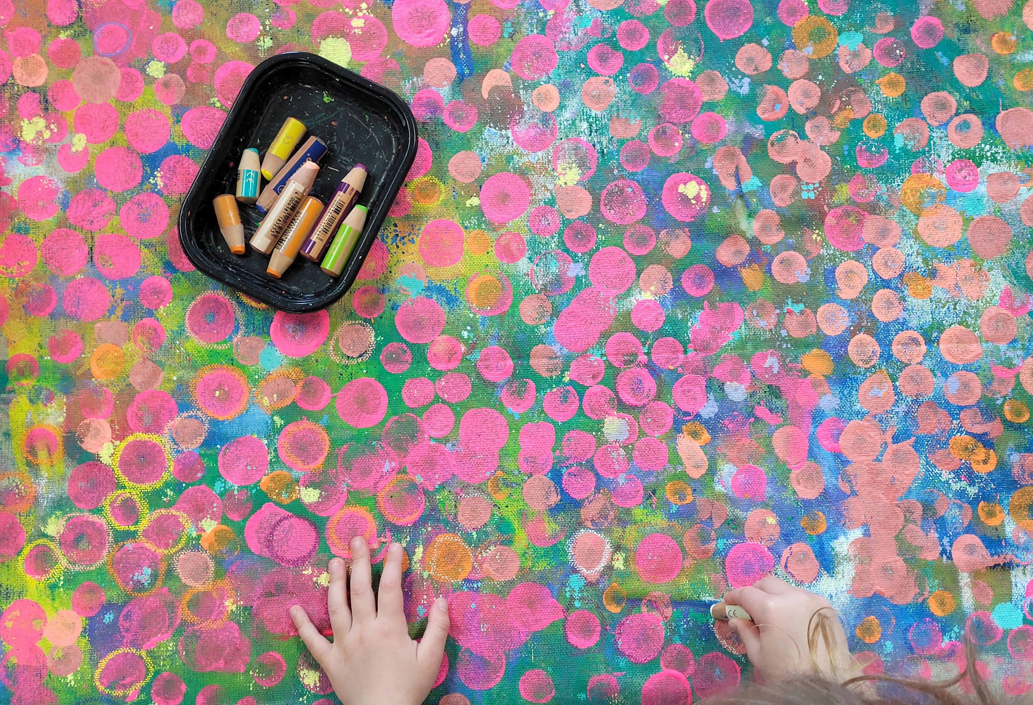 Hands on a colorful painted surface with a tray of art supplies