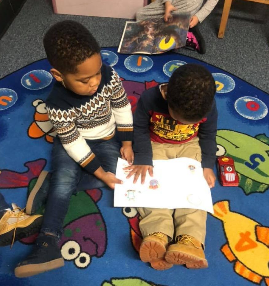 Two children sitting on a rug looking at a paper