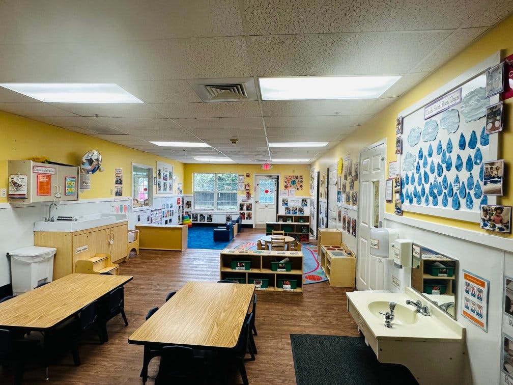 An empty childcare classroom with small tables, chairs, and learning stations