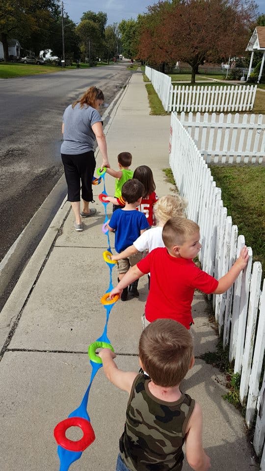 Adult and children walking on a sidewalk holding a colorful rope