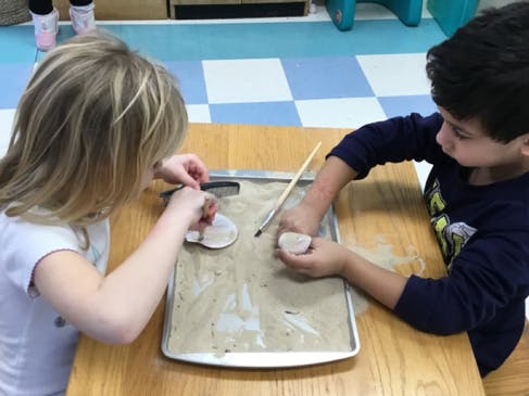 Two children playing with sand and objects on a tray in a classroom