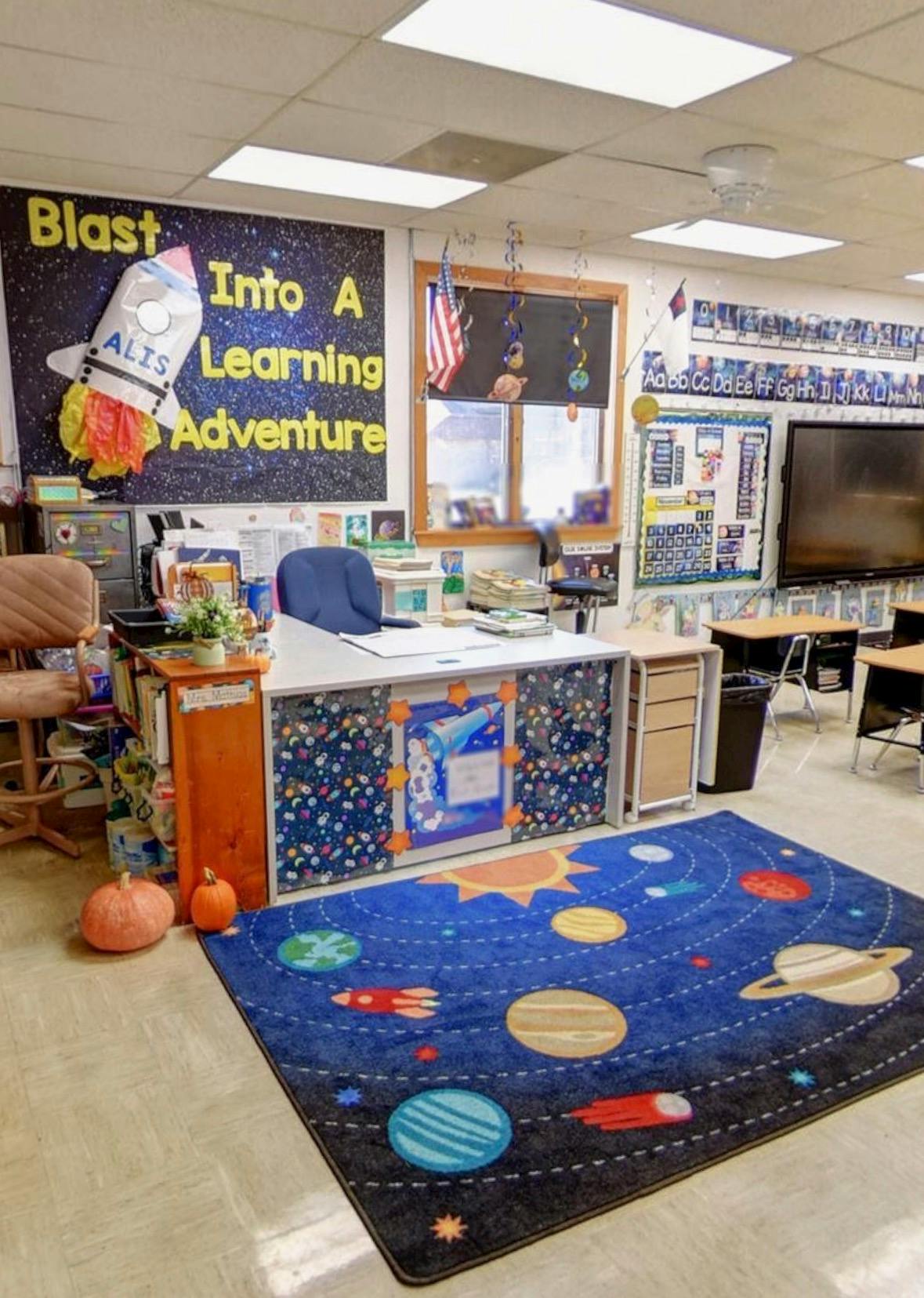 Classroom teacher desk with space themed decorations and a planet rug