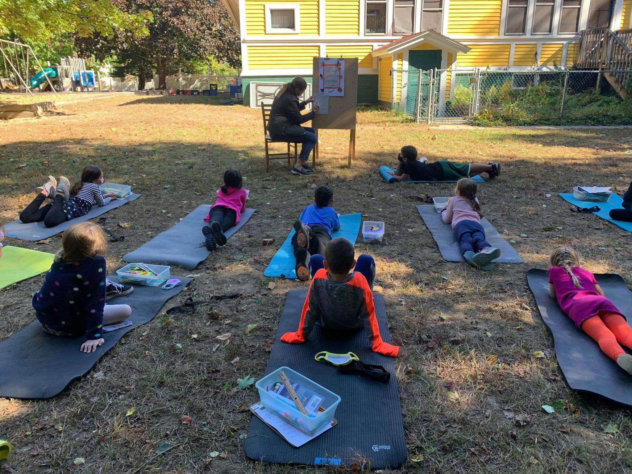 Person teaching children outdoors on yoga mats