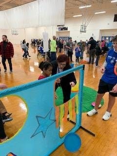 Adult and child playing with a blue activity board in a gymnasium