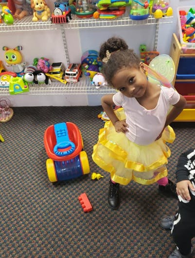 Child in a yellow skirt and white shirt standing in a room with toys