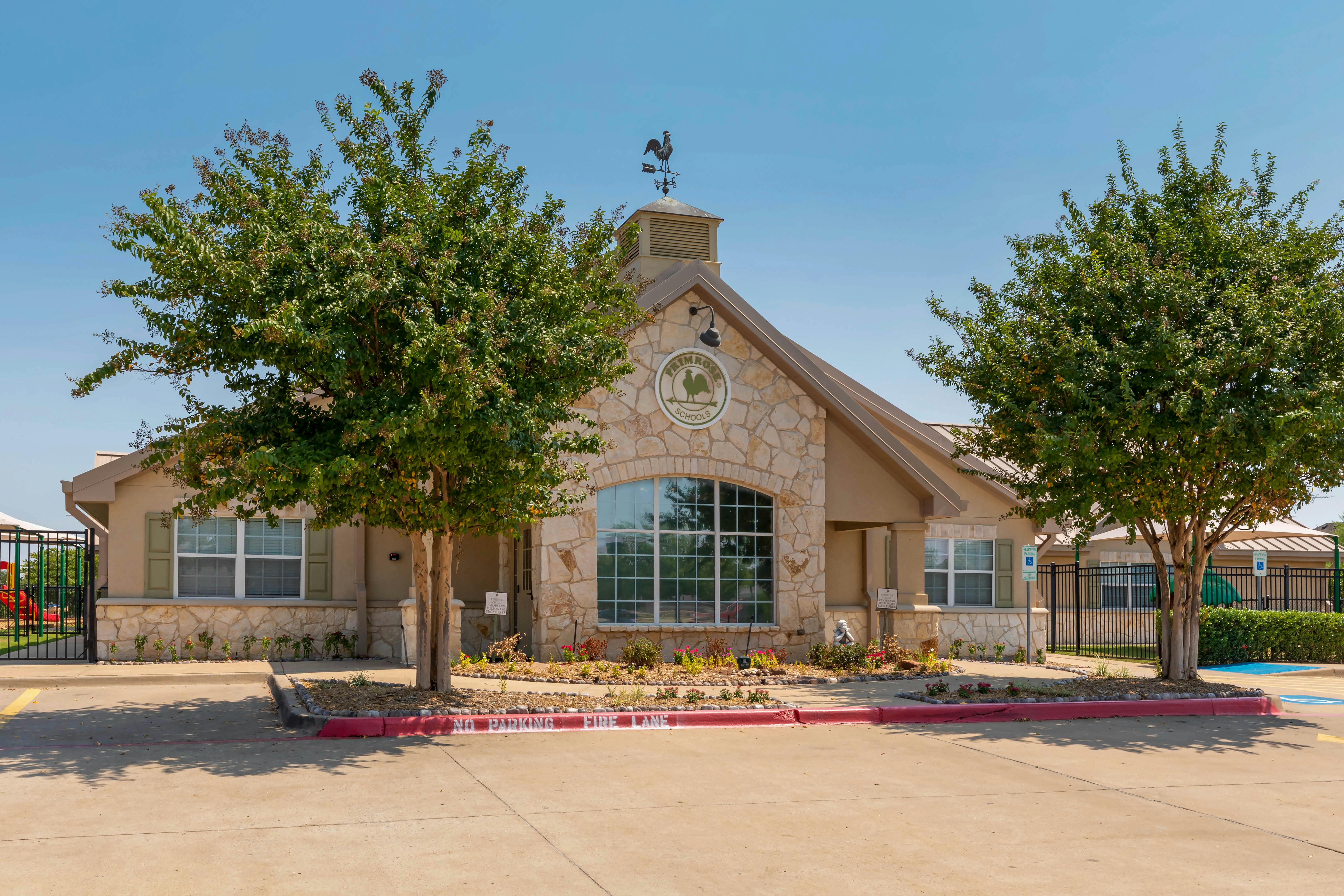 Primrose School building exterior with two trees, a weather vane, and a playground
