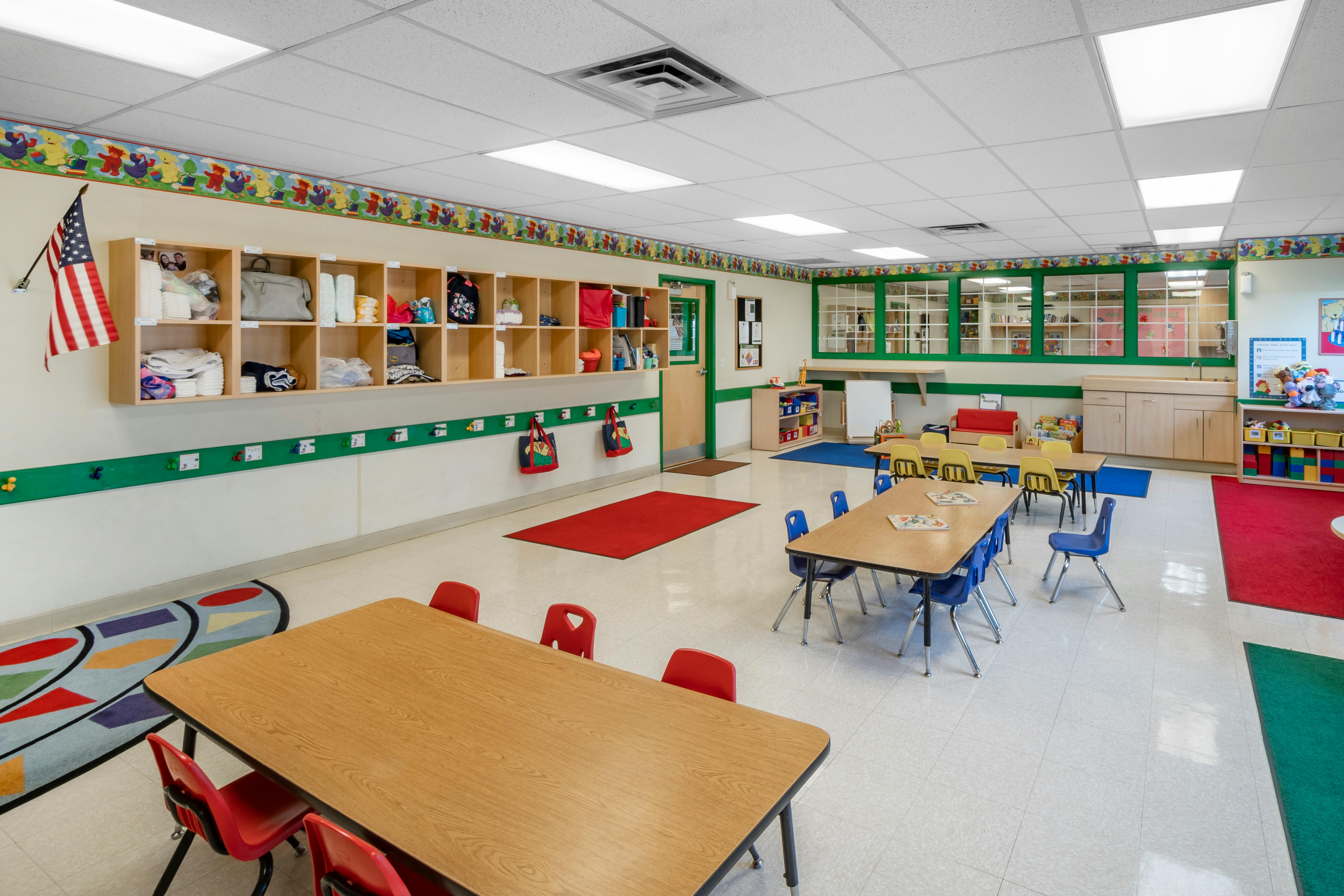 An empty childcare classroom with small tables and chairs arranged, storage cubbies