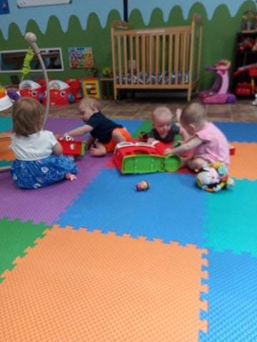 Four children playing with toys on a colorful mat in a room