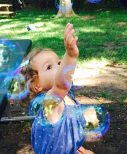 Child reaching up at bubbles outdoors