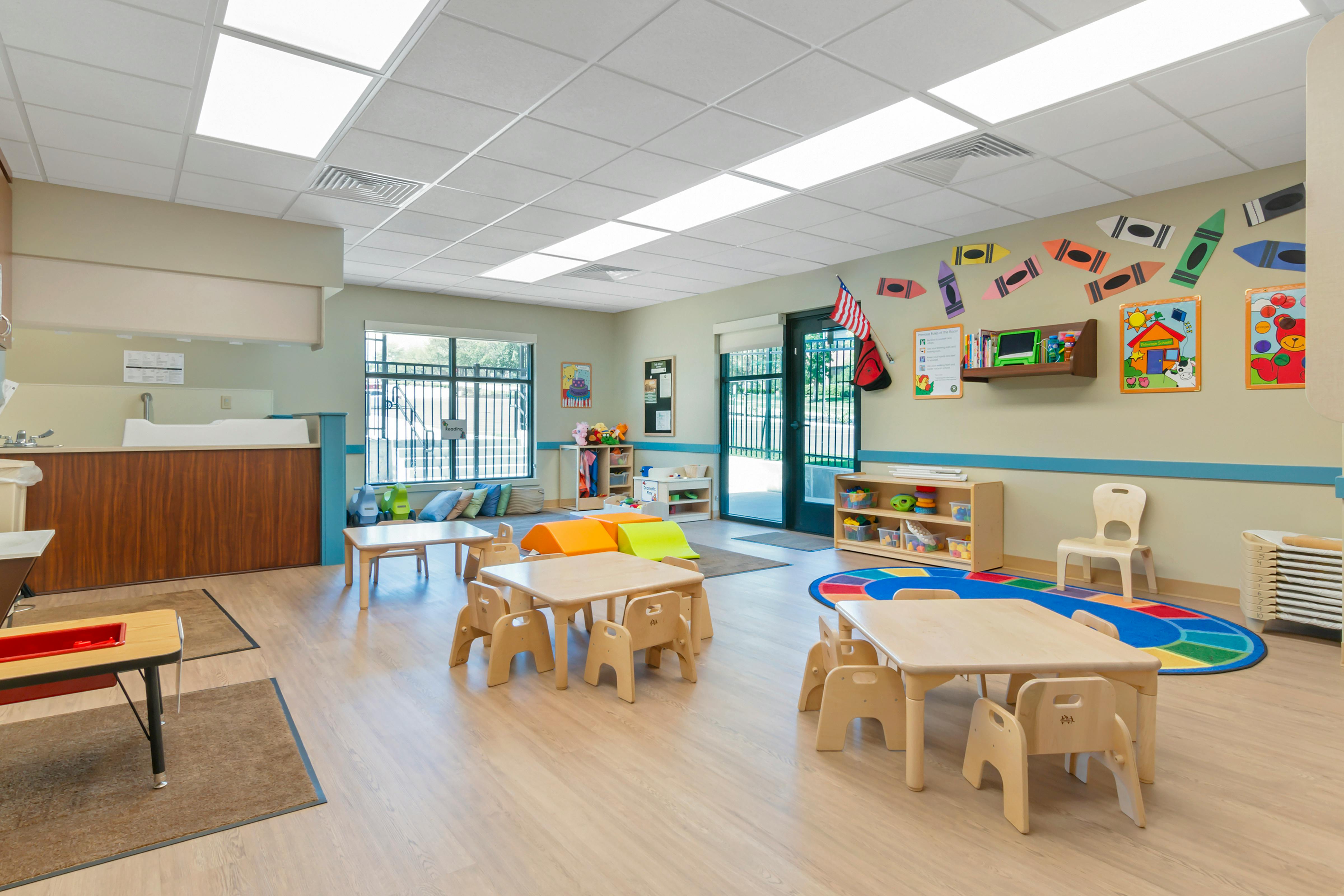 Classroom with small wooden tables and chairs, play mats, and a changing station