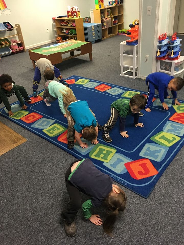 Children on hands and knees on an alphabet rug in a classroom
