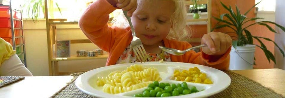 Child eating pasta, peas, and corn with a spoon