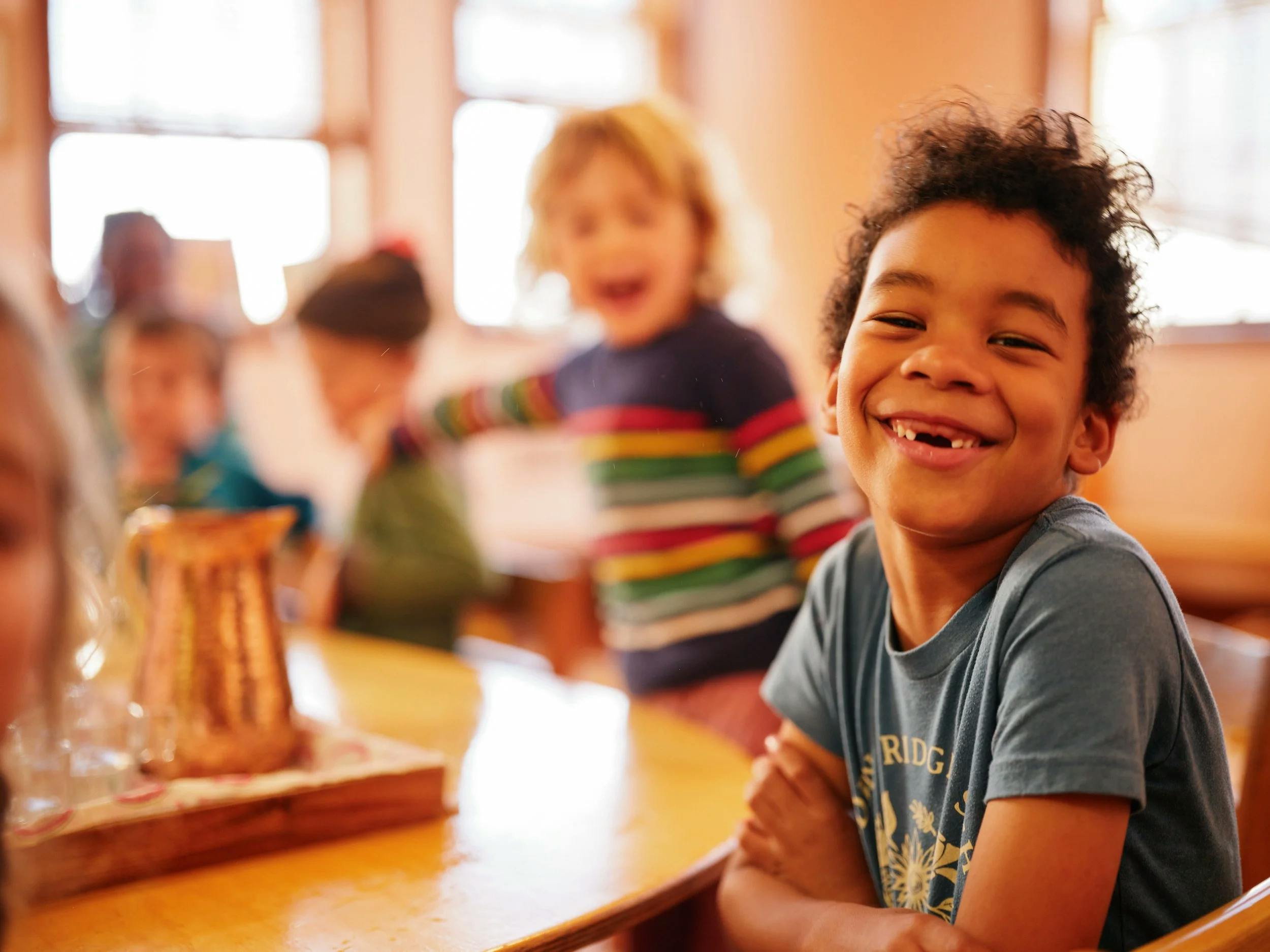 A child in a blue shirt smiling, with another child in a striped shirt behind