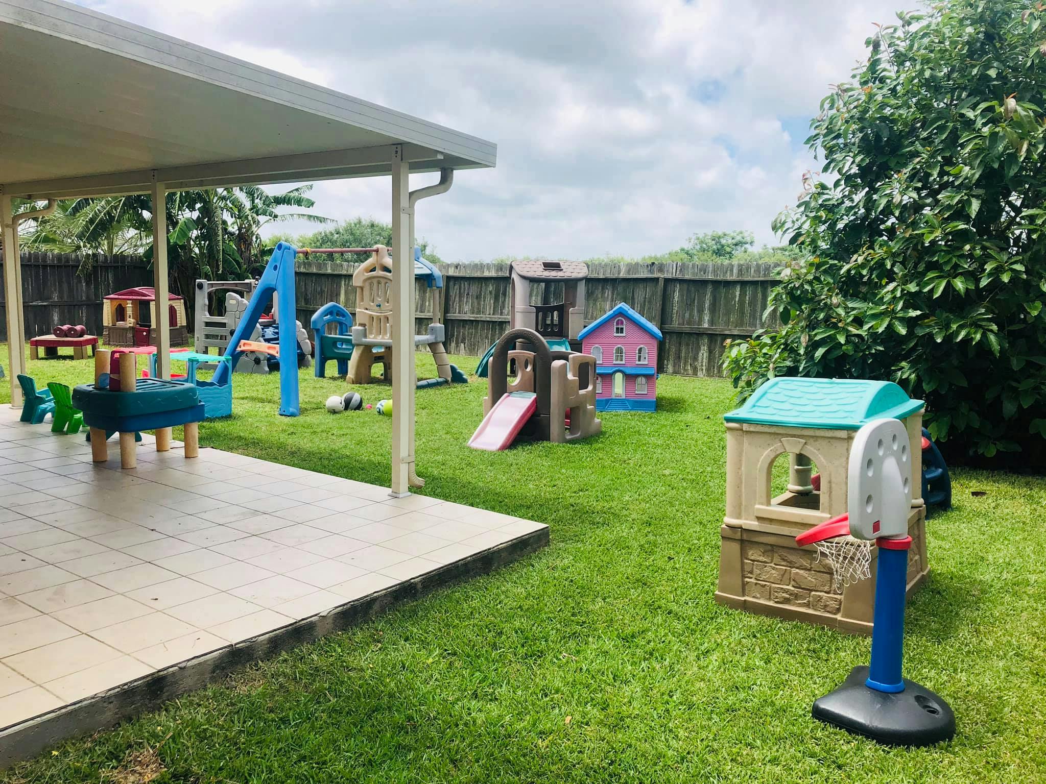 Outdoor play area with various playhouses, slides, and swings on a grassy lawn