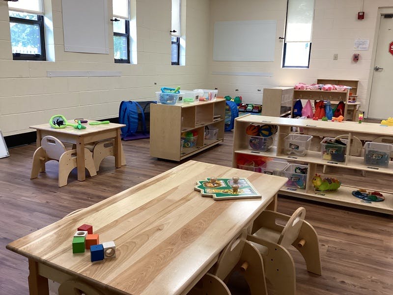 Children's classroom with wooden tables and chairs, shelves of toys