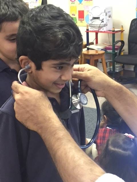 Adult helping a child put on a stethoscope in a classroom