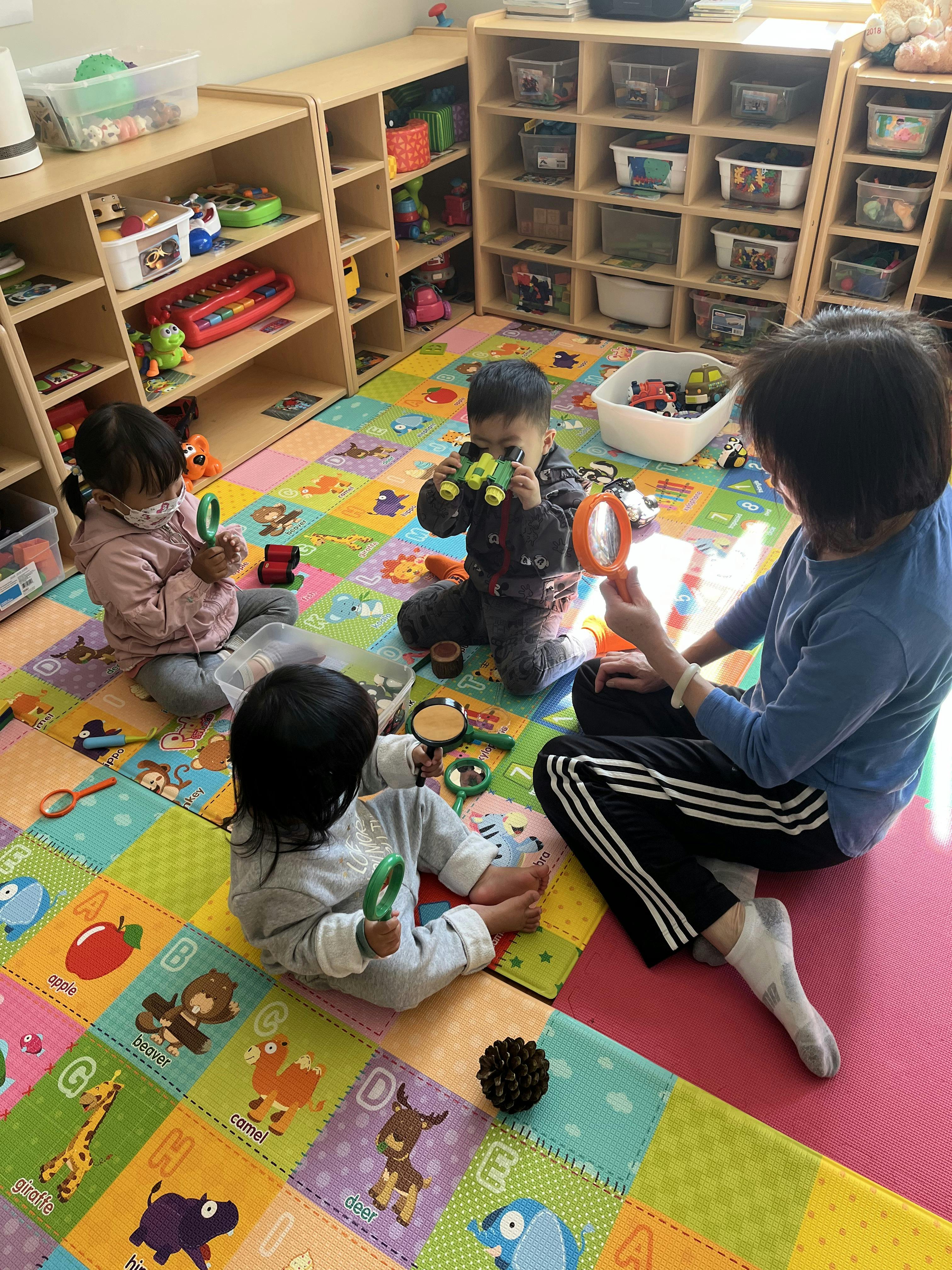 Three children and one adult playing with toys on a colorful mat