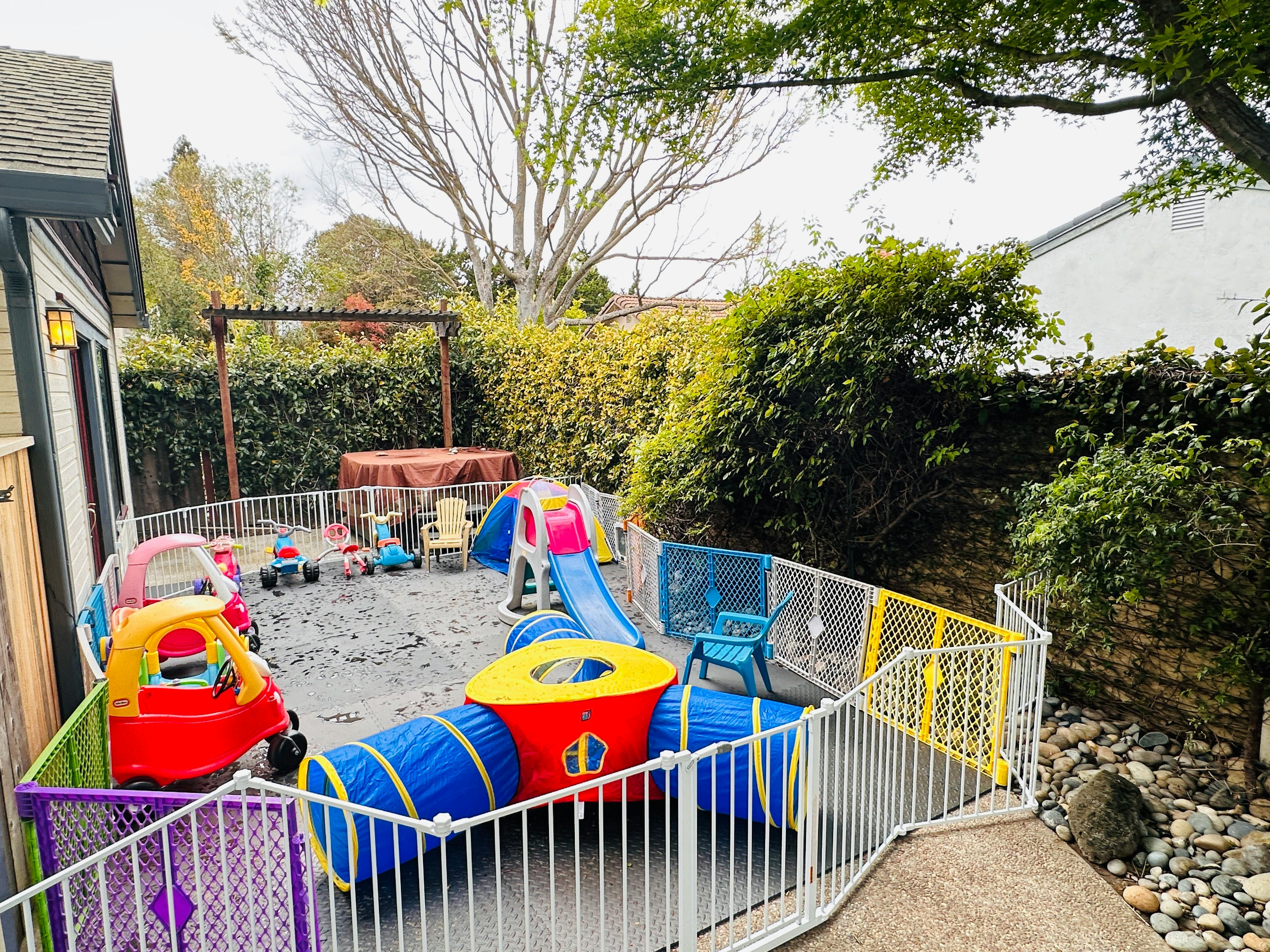 Outdoor play area with slide, tunnel, and toy cars enclosed by a fence
