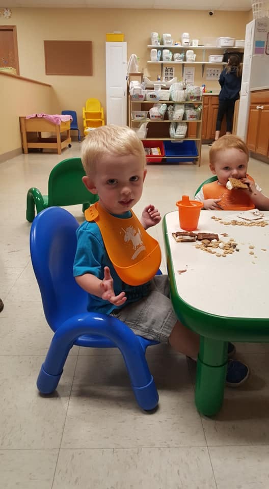 Two children eating snacks at a table in a classroom