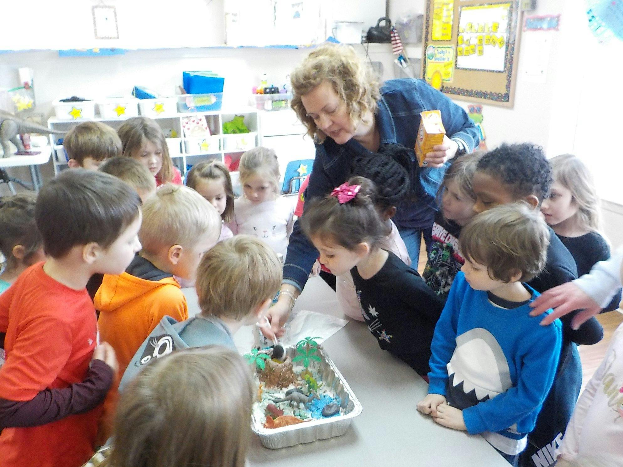 Adult and children gathered around a table looking at a tray of items
