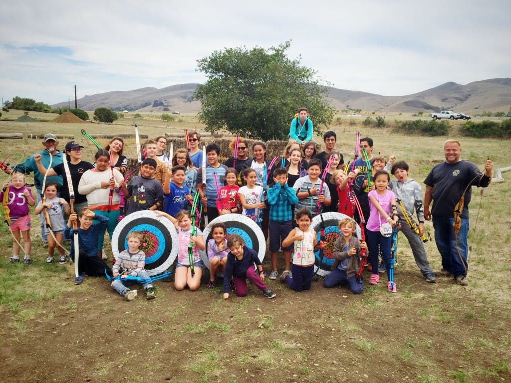 Group of children and adults posing with bows and archery targets outdoors