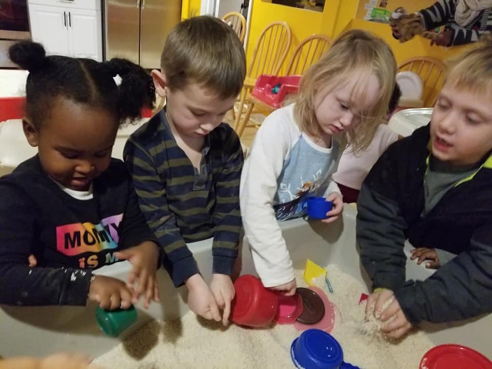 Four children playing with sand and colorful cups