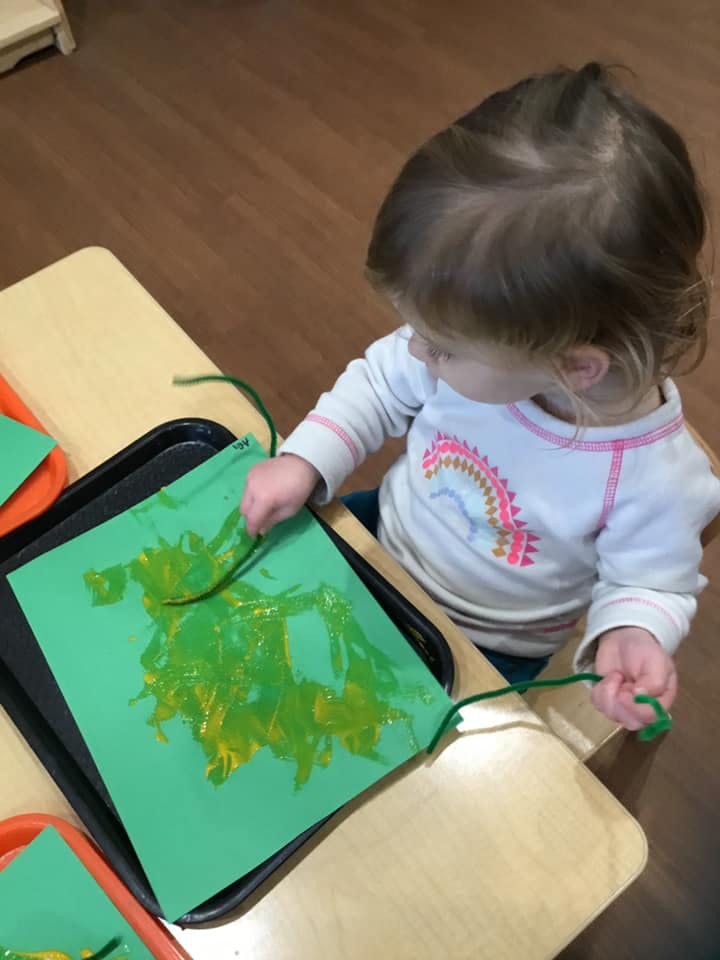Child painting on green paper with a pipe cleaner