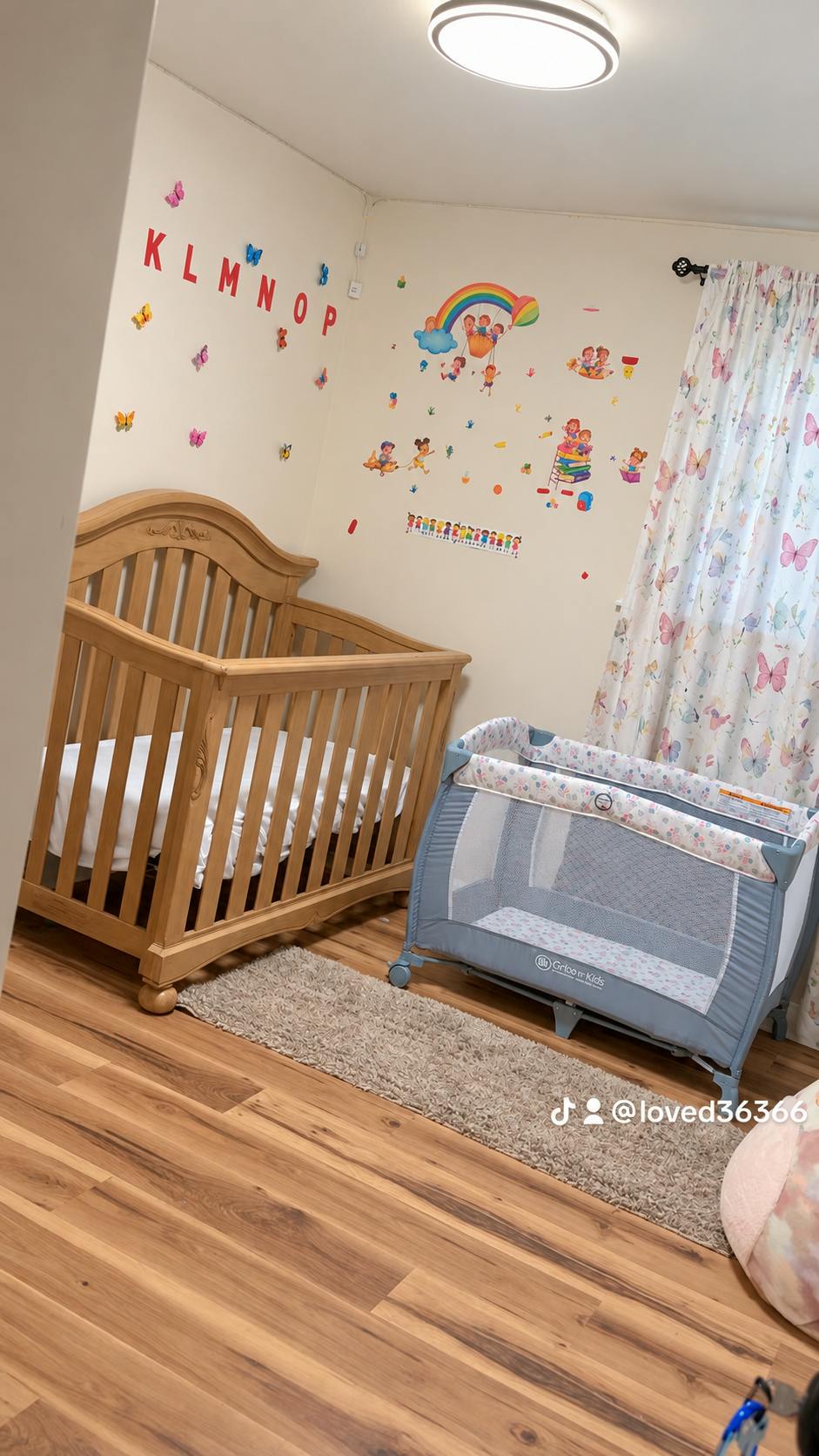 Wooden crib and portable playpen in a nursery with wall decals