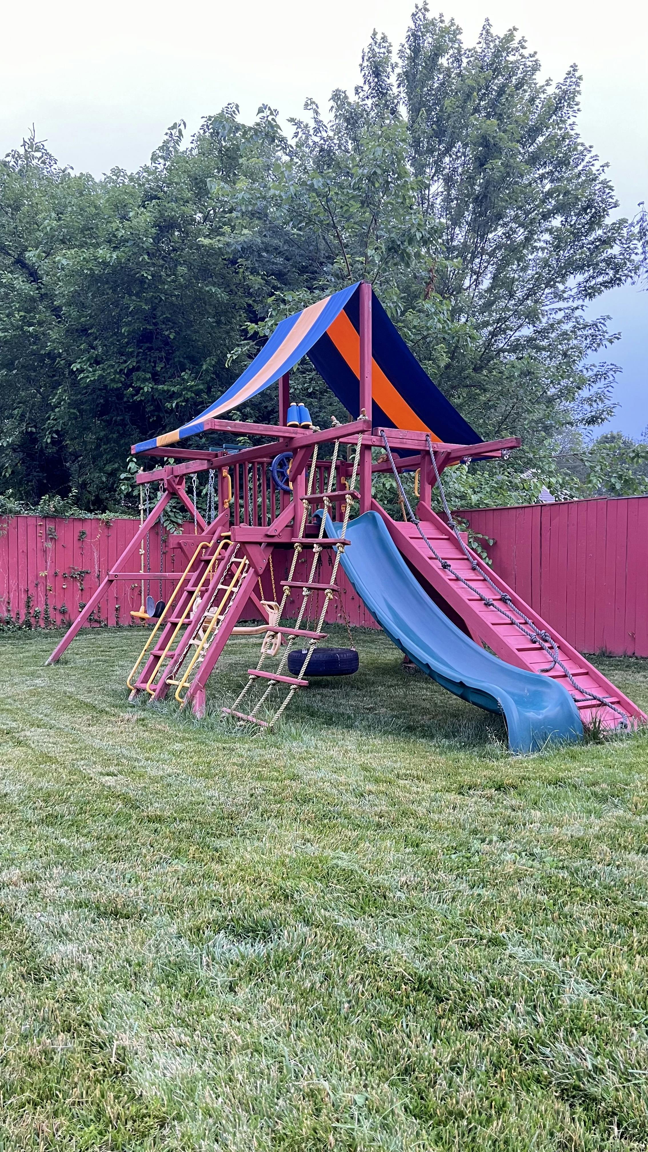 Wooden playset with slides, ladders, and swings in a grassy yard