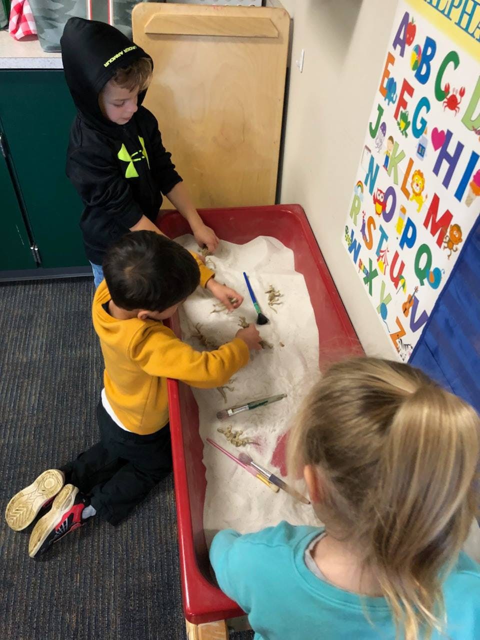 Three children playing with brushes in a sensory bin