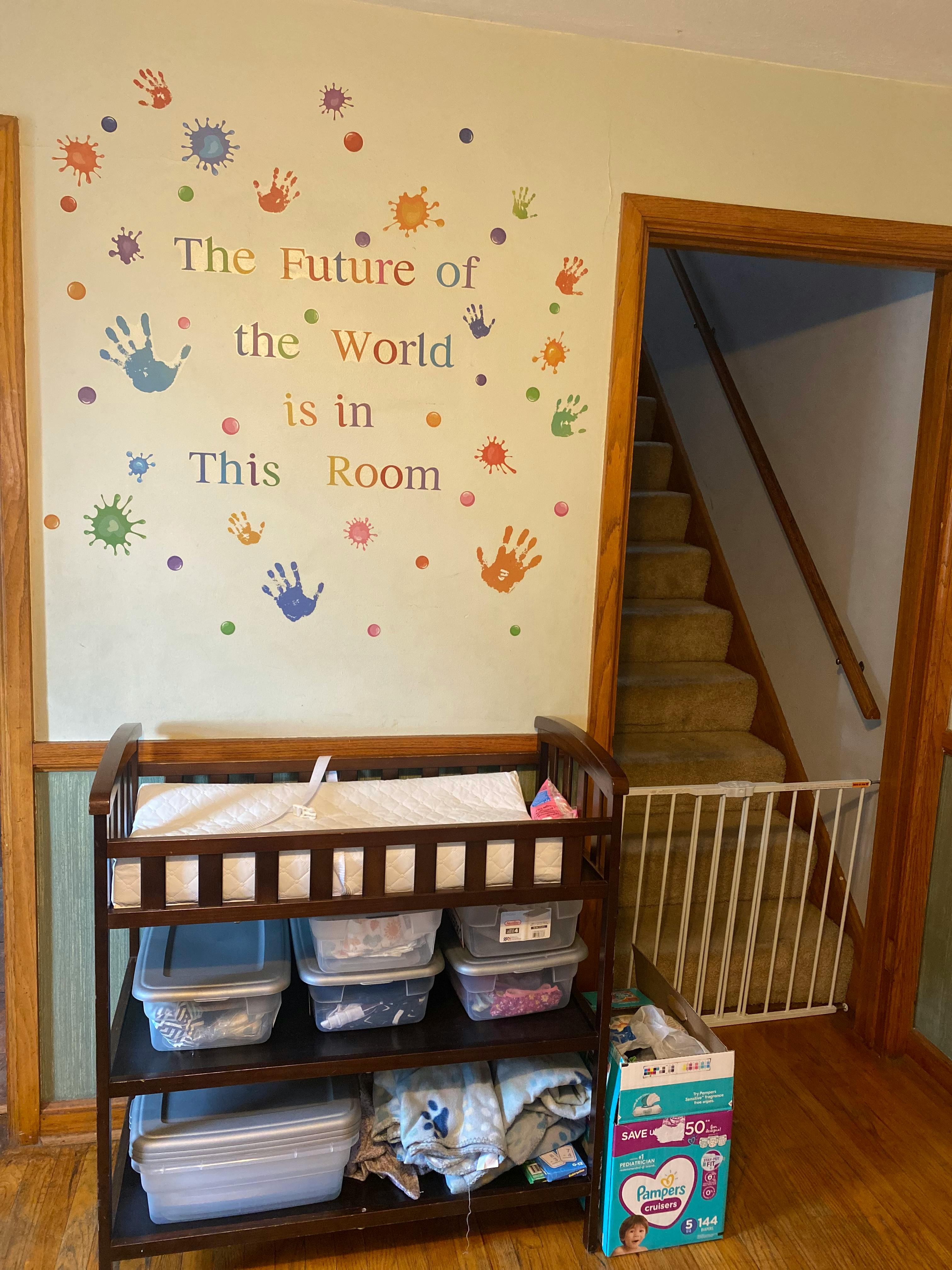 Changing table with storage bins below, wall decor, and stairs with a baby gate