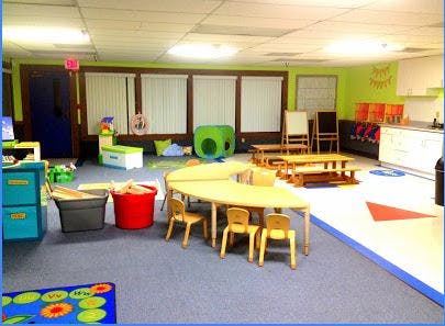 Classroom with small tables and chairs, play tunnel, and storage bins
