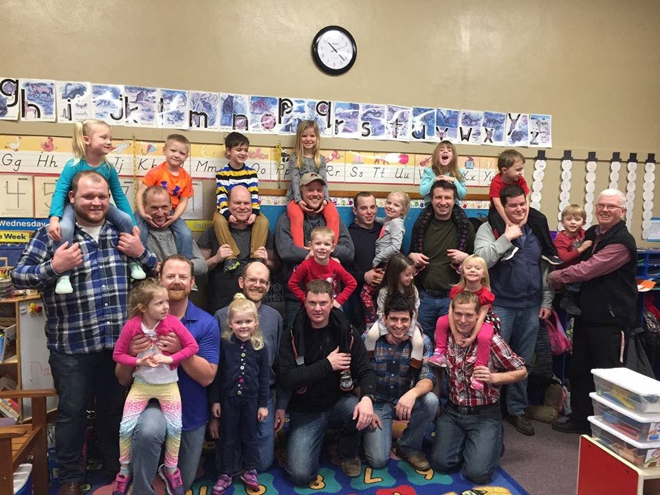 Group of adults and children posing in a classroom, some children on shoulders