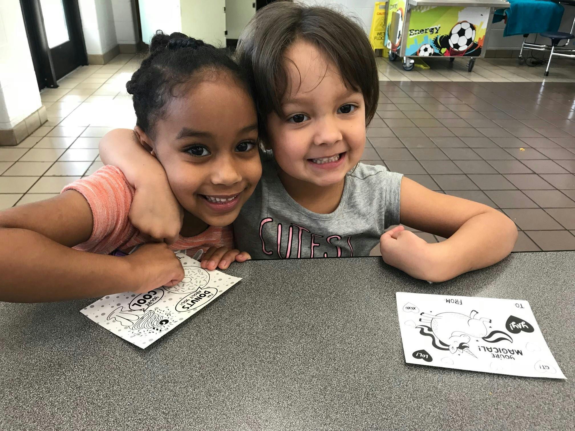 Two children with coloring pages on a table